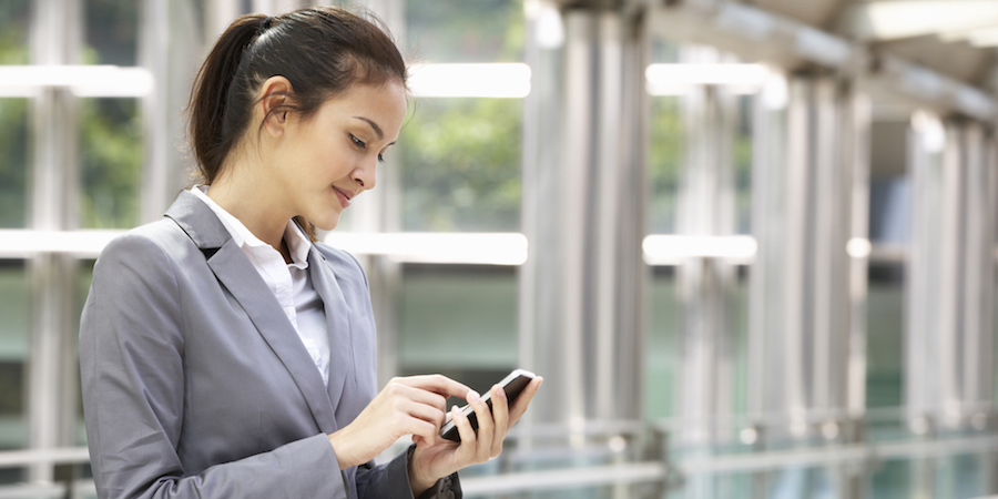 Person using a mobile device outside. The person is wearing a suite and is standing in front of a building.