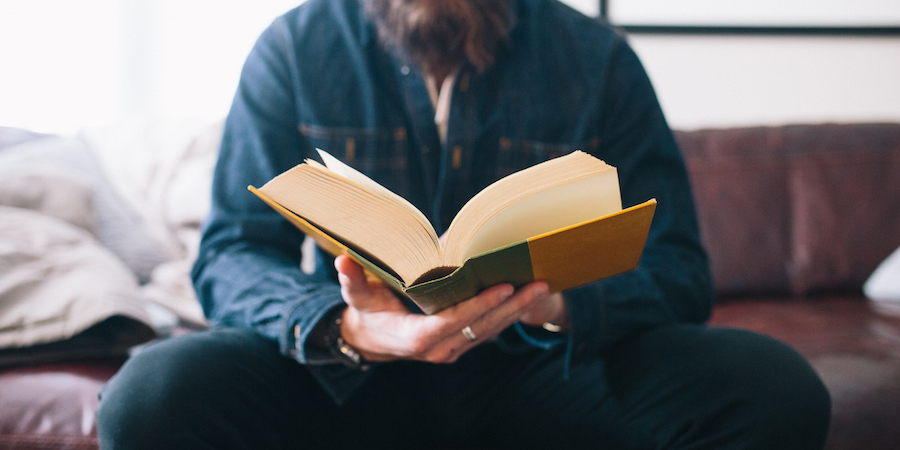 Person reading a large hardcover book on a couch.