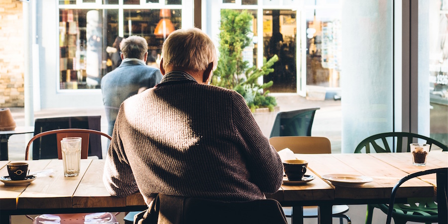 Person sitting at a restaurant table. There are glasses and mugs on the table suggesting others were just there. You can see outside to a street.