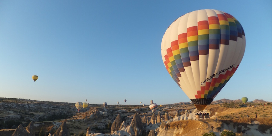 Hot air balloons floating over a desert. One balloon says Rainbowballoons.net.