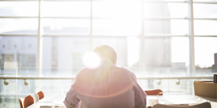 Back side of a person sitting at a conference table. In front of them is a large window with a lens flare effect.