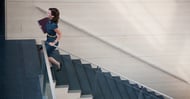 Person carrying a laptop walking up a flight of stairs.