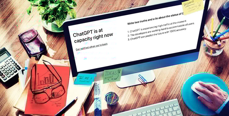iMac on a wood desktop with text on its screen saying "ChatGTP is at capacity right now. Get notified when we're back."