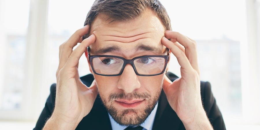 Person in a suite wearing glasses holding their head and looking worried.
