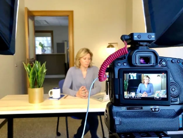 Nicole Mertes sitting at a desk in front of a camera and studio lights.