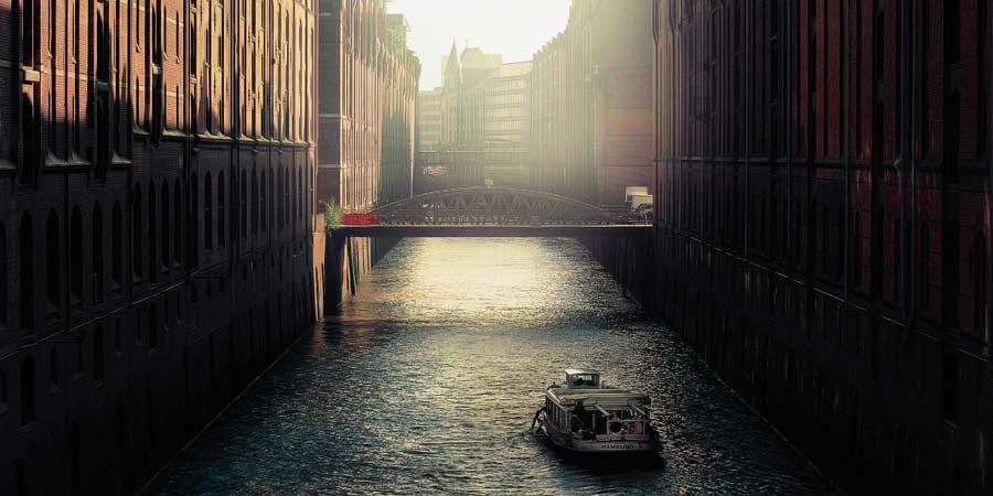 River in a city with a tour boat traveling down it. There are two bridges in the distance.