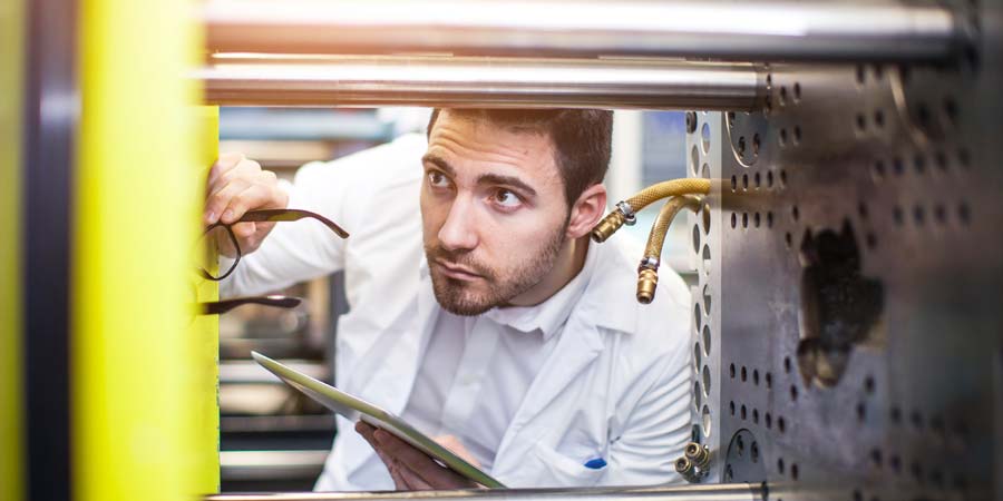 Worker in a lab coat inspecting a injection molding machine.