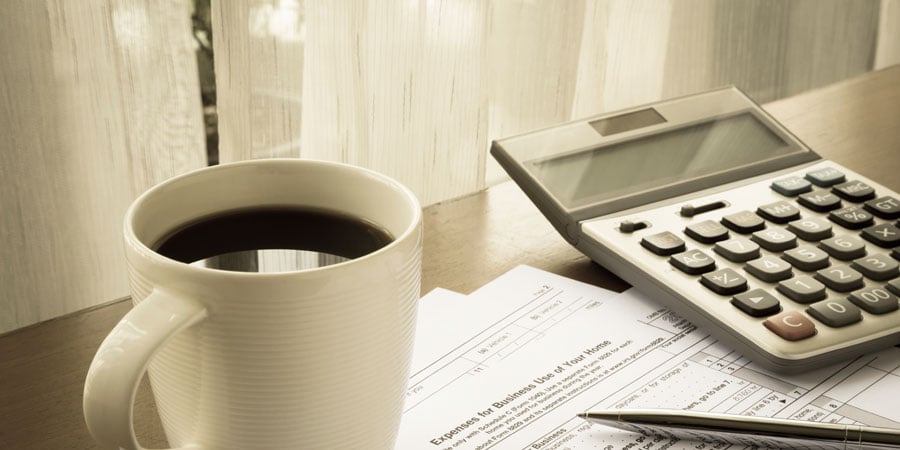 Full coffee cup, calculator, and tax forms sitting on a desk.
