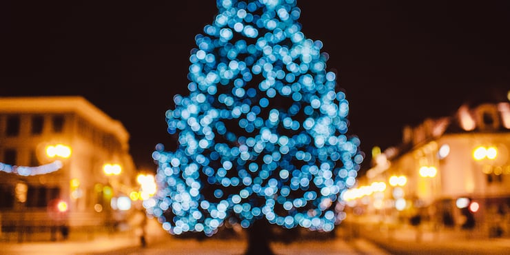 Blurry Christmas tree with blue lights on it in the center of a town square
