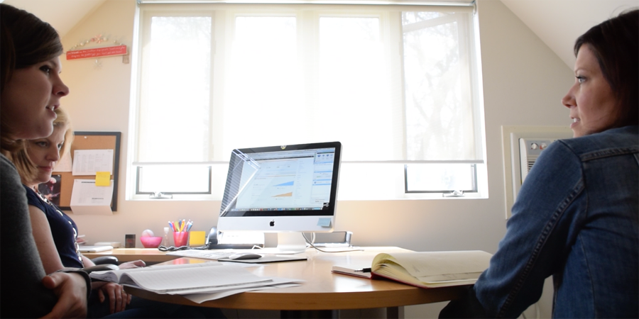Three Weidert employees sitting at an office desk with an iMac on it. There is a bright window in the background.