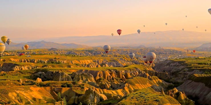 Hot air balloons floating over an arid landscape with low mountains in the background.