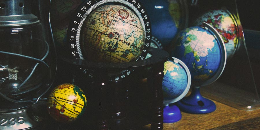 Collection of different globes with different colors and styles of maps on them sitting on a shelf.