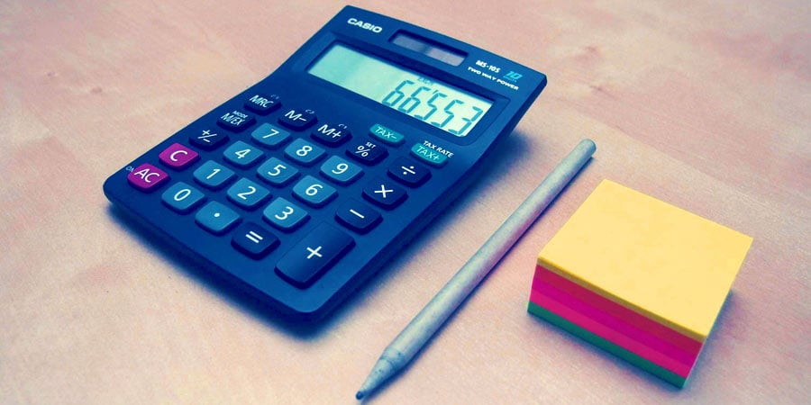 Calculator, pen, and stack of post-it notes on a desk.