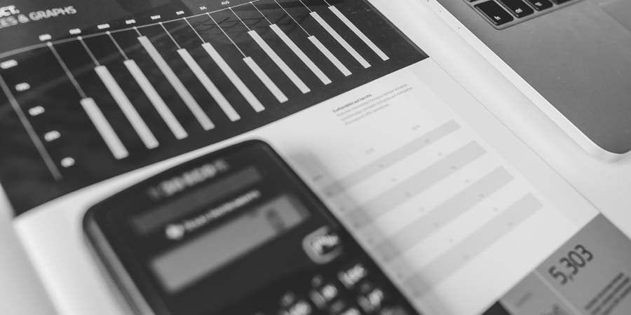 Brochure with graphs and tables sitting underneath a calculator next to a laptop.