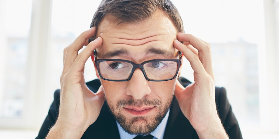 Person in a suite wearing glasses holding their head and looking worried.